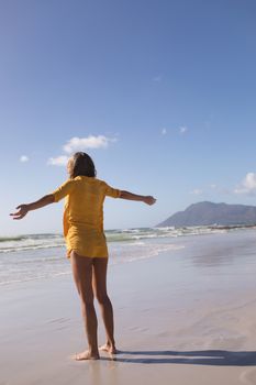 Rear view of woman standing with arms outstretched at beach in the sand