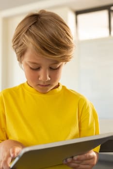 Front view of cute Caucasian boy using digital tablet in a classroom at elementary school