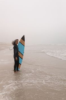 Side view of senior female surfer with surfboard standing on the beach