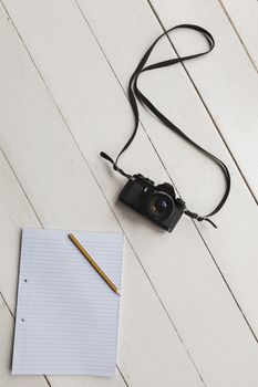 Overhead view of a notepad, pencil and camera placed on the floor at home
