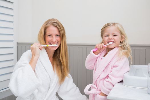 Happy mother and daughter brushing their teeth at home in the bathroom