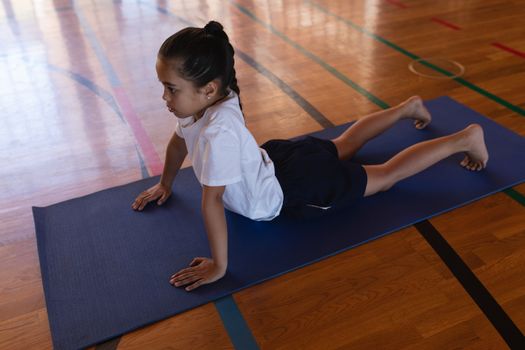 Side view of schoolgirl doing yoga on a yoga mat in school gymnasium