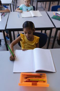 High angle view of schoolgirl writing on notebook at desk in classroom of elementary school