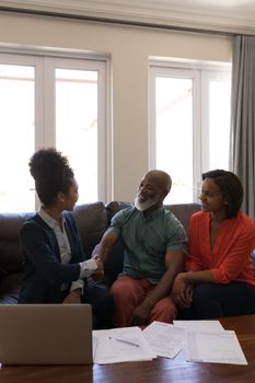 Front view of a female real estate agent shaking hands with a senior man while sitting on the sofa in living room at home