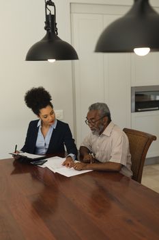 Side view of a senior African American  man and real estate agent discussing over documents on the table in living room at home