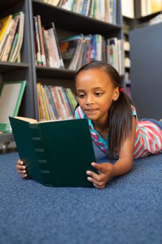 Front view of a mixed-race schoolgirl reading a book in the library at school
