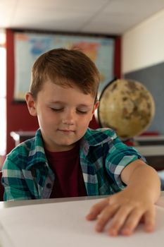 Front view of Caucasian blind boy reading a braille book at desk in classroom at elementary school