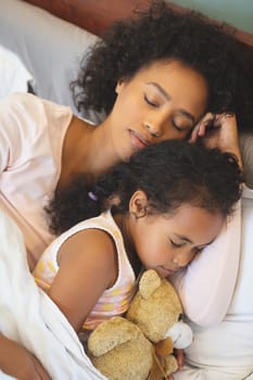Close-up of African American mother and daughter sleeping together on bed in bedroom at home