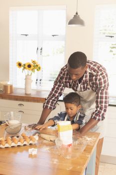 Front view of African American father and son rolling out cookie dough in kitchen at home