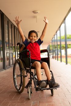 Front view of happy mixed-race disabled schoolboy with arms up looking at camera in corridor at elementary school