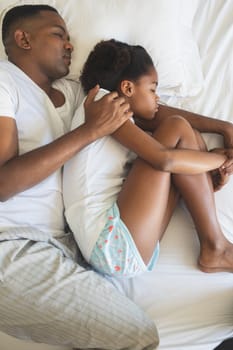 High angle view of African American father and daughter sleeping together on bed in bedroom at home