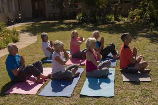 Side view of trainer training senior people in performing yoga on yoga mat at park