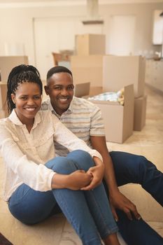 Front view of happy African American couple sitting on floor and looking at camera in a comfortable new home