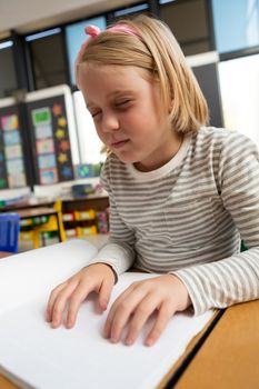 Side view of a blind Caucasian schoolgirl reading a braille book at desk in the classroom at school