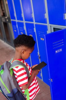 High angle view of a cute African American schoolboy holding mobile phone in the locker room