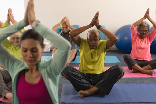 Front view of senior people doing yoga with female trainer in fitness studio