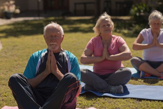 Front view of active senior people performing yoga on yoga mat in the park