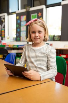 Portrait of a Caucasian schoolgirl using digital tablet while looking at the camera in the classroom at school