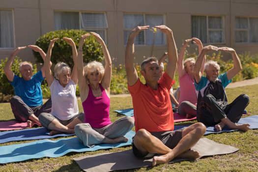 Front view of trainer training senior people in performing exercise on yoga mat at park