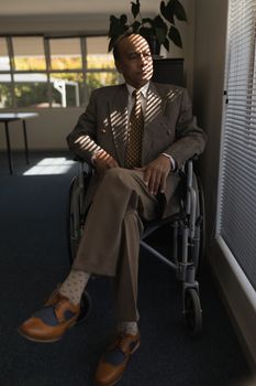 Front view of disabled senior man sitting on wheelchair and looking outside through window at home