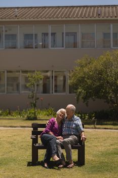 Front view of active senior couple sitting together and doing cuddle on the bench in the park