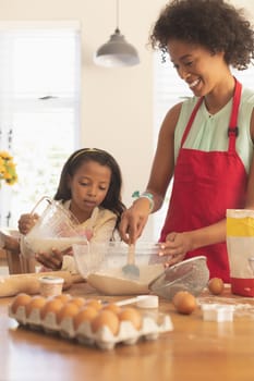 Front view of African American mother and daughter mixing cookie dough ingredients together in kitchen at home