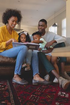 Front view of happy African American parents with their cute children reading storybook on the sofa in a comfortable home