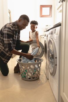 African American father and son washing clothes in washing machine at home