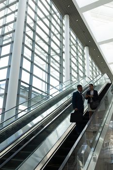 Side view of businessman and businesswoman interacting with each other while moving down on escalator in office