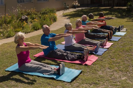 Side view of group of active senior people exercising aligned on yoga mat in the park