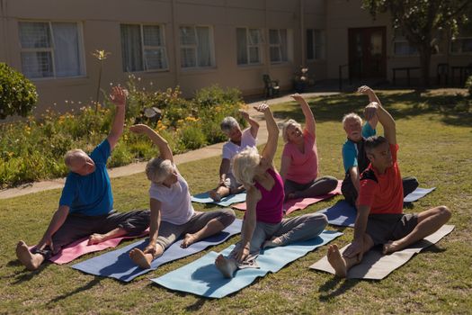 High angle view of trainer training motivated senior people in performing exercise on yoga mat at park