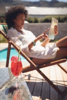 Close-up of glass of cocktail on table while woman using digital tablet in background on a sunny day
