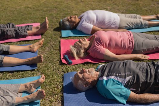 How angle view of group of active senior people performing yoga posistion on the back on yoga mat in the park
