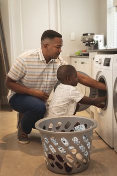 Side view of African American father and son washing clothes in washing machine at home
