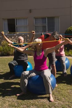 Front view of trainer assisting senior women in performing exercise with elastic band and ball in the park