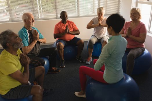 Front view of female trainer training senior people in performing yoga with ball exercice  at home