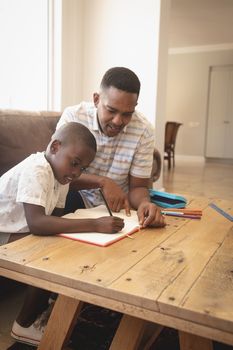 Front view of African American father helping his son with homework at table in a comfortable home