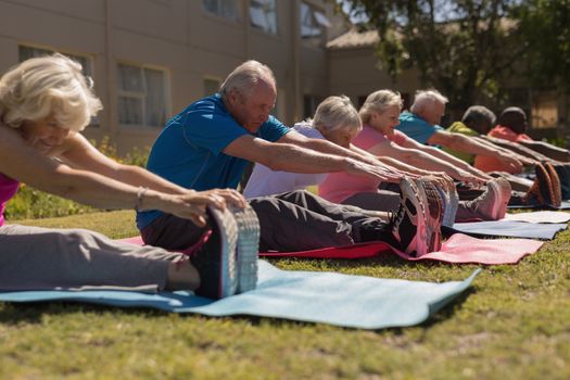 Side view of group of active senior people exercising and scretching ones legs on yoga mat in the park