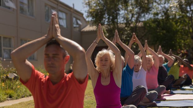 Front view of senior group concentrated doing yoga together in the park on a beautiful sunny day. They are at peace and sitting on yoga mat.