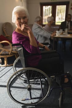 Side view of disable senior woman sitting on whee chair and looking at camera in home