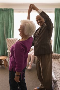 Side view of happy senior couple dancing with woman turning together at home
