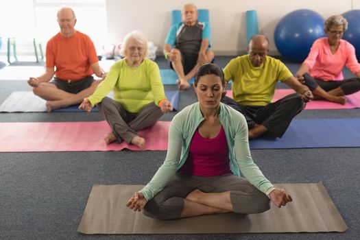 Front view of senior people doing yoga with female trainer in fitness studio