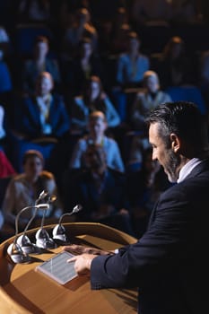 High angle view of Caucasian businessman standing and looking at digital tablet on stage in auditorium