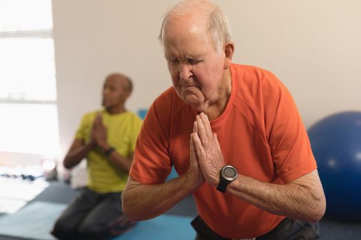 Front view of senior woman doing yoga on the foreground with his friend behind his in fitness studio