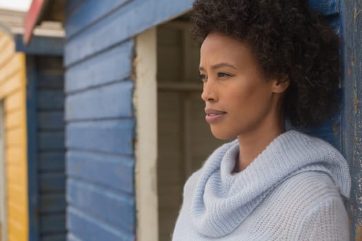 Side view of thoughtful young African American woman leaning standing against beach hut. She is looking away 