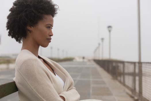 Side view of thoughtful young African American woman sitting on bench at promenade 