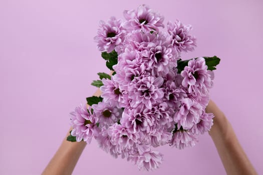 Front view of woman holding a bouquet of pink flower between her hands with pink backdrop for valentines day