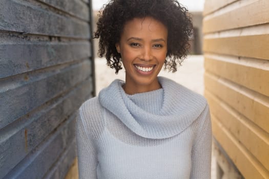 Portrait of happy young African American woman standing at beach hut. She is smiling and looking at camera