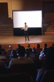 High view of young Asian businessman standing and giving presentation in auditorium while holding mike in his hand in auditorium