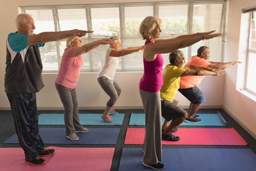 Side view of group of active senior people performing exercise on yoga mat at home